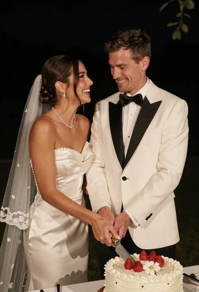 Joyful bride and groom cutting wedding cake at night reception