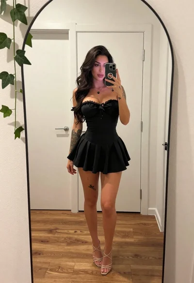 Young woman taking mirror selfie in black dress indoors