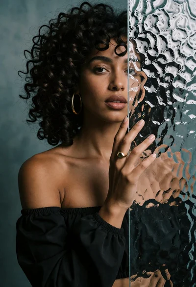 Woman peeking from behind a rippled translucent panel against grey wall