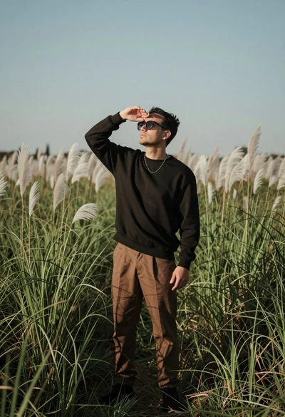 Man in black sweatshirt standing in tall green grass shielding eyes from
