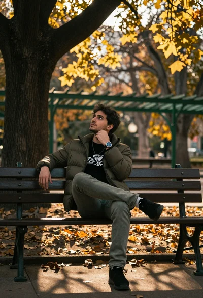 Young man sitting thoughtfully on park bench under golden sunlight filtering through