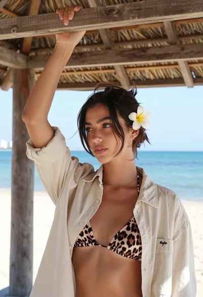 Young woman in beige shirt under thatched roof overlooking turquoise ocean