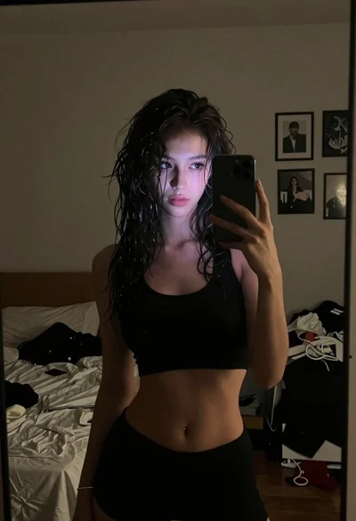 Woman with dark wavy hair taking mirror selfie in bedroom