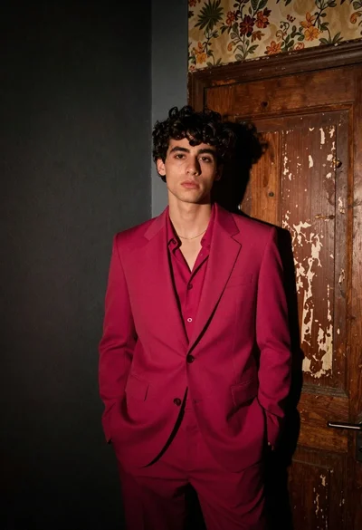 Young man in magenta suit jacket standing in dimly lit room with