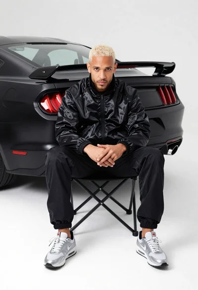 Man in black track jacket sits on chair in front of matte