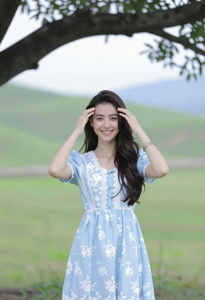 Smiling young woman in blue floral dress standing under tree branch