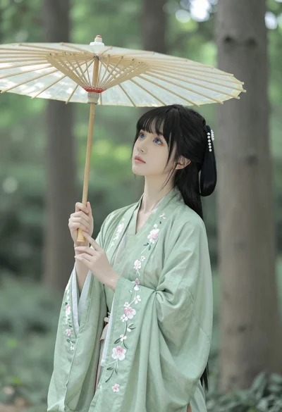 Young woman in sage green hanfu robe holding parasol in sunlit forest
