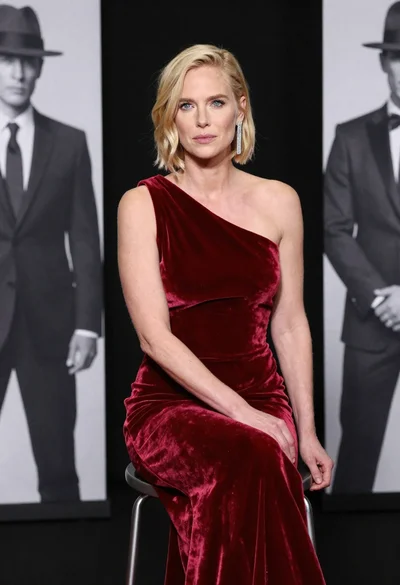 Blonde woman in deep red velvet gown sitting on stool studio portrait