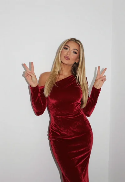 Fair blonde woman in deep red velvet dress posing against plain white