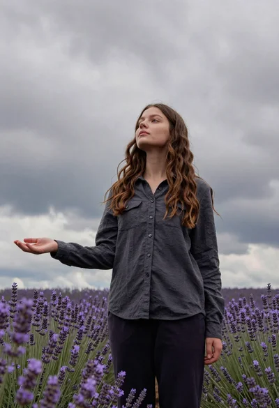 Young woman in dark shirt standing in purple lavender field under cloudy