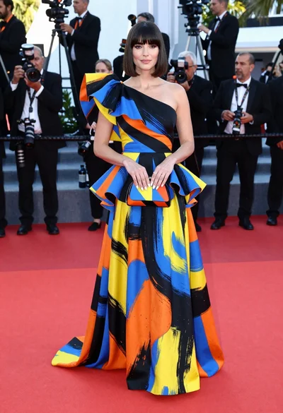 Woman in colorful oneshoulder gown standing on red carpet at event