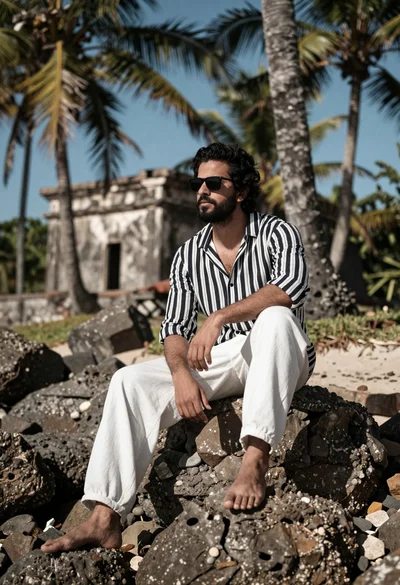 Man seated on rock at tropical shoreline near old stone structure