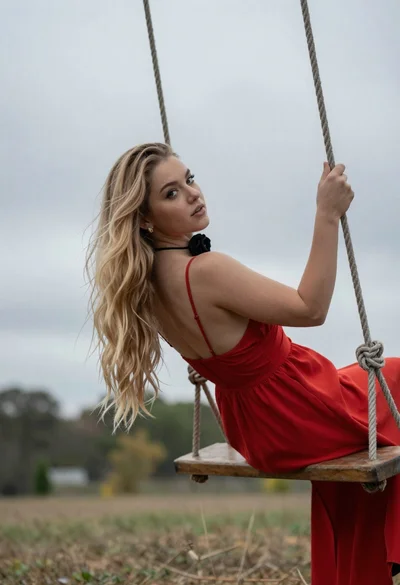 Blonde woman in red dress swinging outdoors under cloudy sky