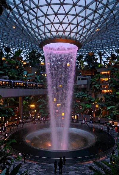 Massive indoor waterfall cascading into pool surrounded by tropical greenery and people