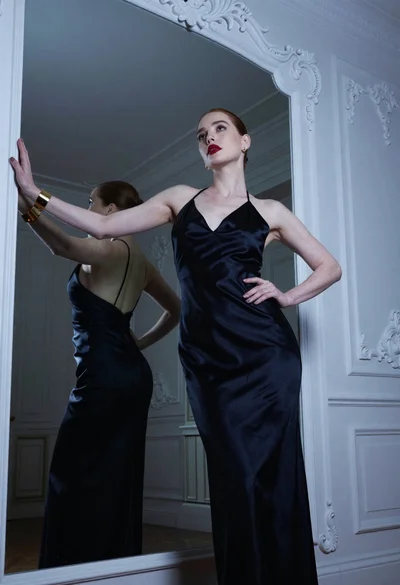 Fair skinned woman in black gown before ornate mirror with blue lighting