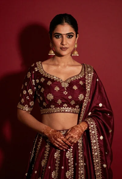Confident woman in maroon lehenga choli with gold embroidery against red background