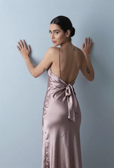Woman in dusty rose slip dress looking over shoulder against light blue