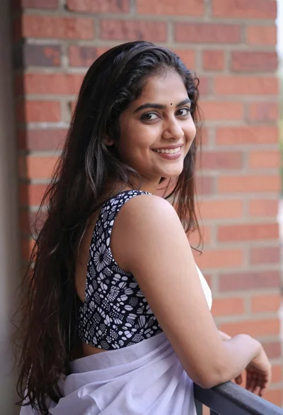 Young woman with dark hair smiling over shoulder against red brick wall