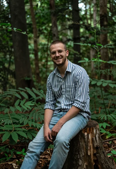 Young man in striped shirt sitting on tree stump in lush forest