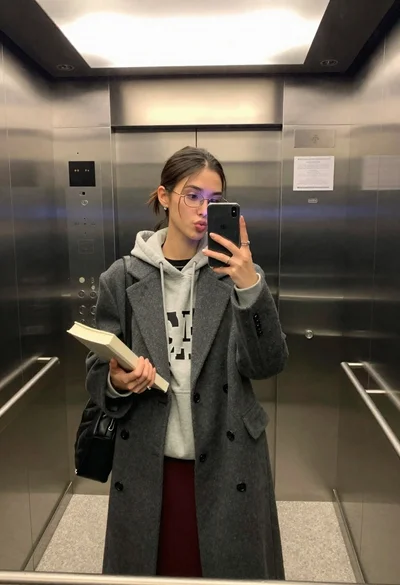 Young woman taking a mirror selfie in an elevator holding a book