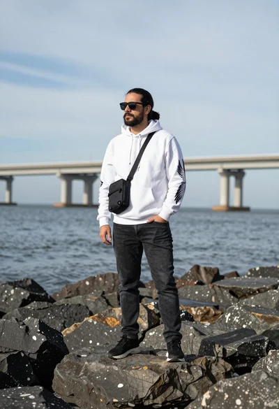 Man standing on dark rocks near ocean with large bridge background