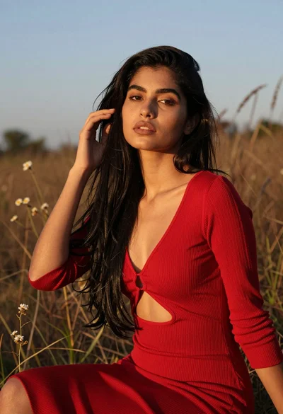 Young woman with black hair in red dress field at golden hour