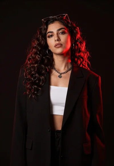 Confident woman with dark wavy hair in black blazer against red backlight