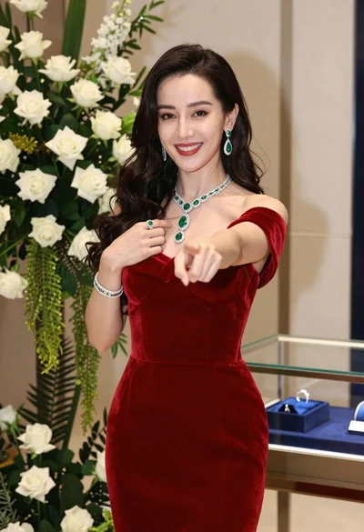 Confident woman in red velvet dress with diamond emerald jewelry indoors