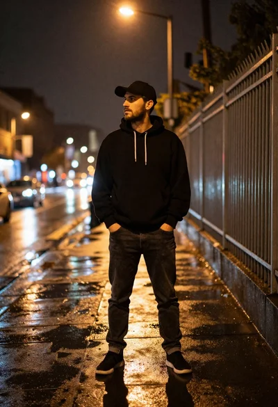 Young man in black hoodie standing on wet city sidewalk at night