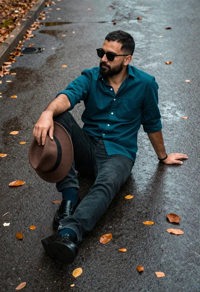 Man sitting on wet asphalt surrounded by fallen brown leaves at low