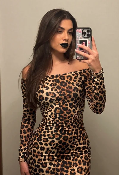 Woman taking a mirror selfie in leopard print dress against light wall