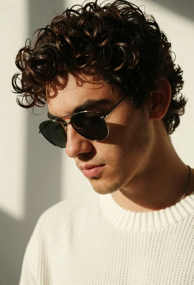 Portrait of young man with curly hair and sunglasses in white sweater